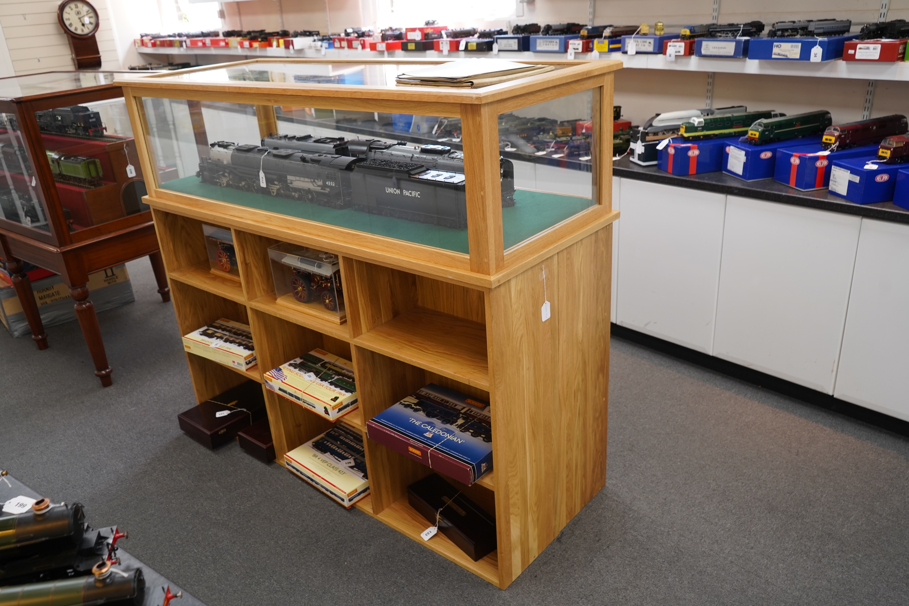 An engineered oak display stand, with a removable glazed top, and double sided base divided into nine compartments on each side, dimensions; 160cm wide, 60cm deep, 141cm high (contents for display purposes only and not i